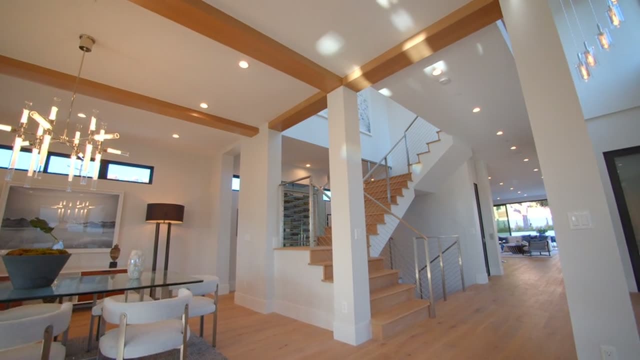A cinematic interior of a finished modern home — open-plan living, an oak staircase and full-height glazing.